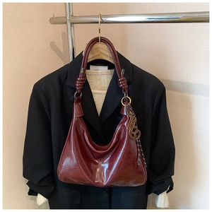 Detail of burgundy glossy leather hobo bag with knotted strap on wooden hanger