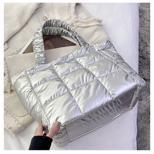 Close-up of metallic silver quilted tote bag with ruched handle on textured background