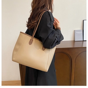 Detail view of large beige leather tote bag with brown contrast trim on model