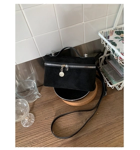Detail of black matte suede handbag with metal zipper and circular charm accessory