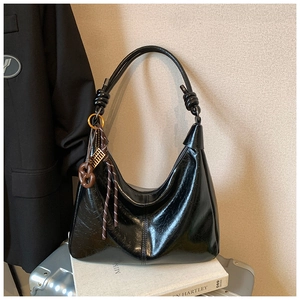 Detail of black glossy hobo bag featuring stylish knot handle and decorative charms