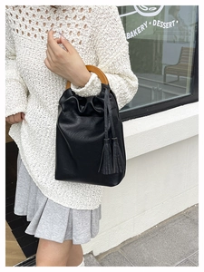 Detalle del bolso cubo negro con asa redonda de madera y colgantes de borlas