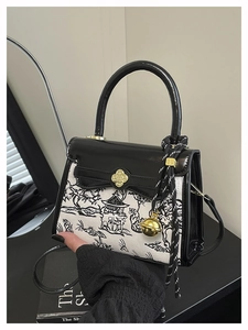 Detail of canvas handbag with mountain print, black flap, and golden clover buckle clasp