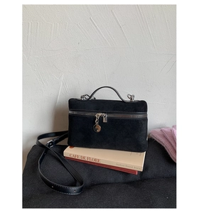 Detail of black suede square handbag with silver zipper on a minimalist book stand