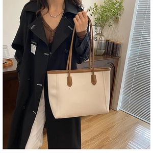Detail of minimalist cream tote bag with brown handles on a model in dark coat