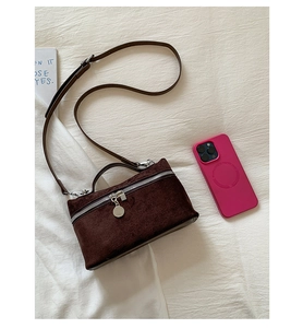Detail of dark brown suede crossbody box bag with silver zipper and pink phone for scale