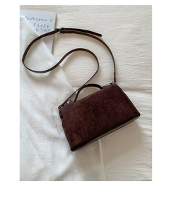 Detail view of a dark brown suede crossbody bag with handle on beige fabric