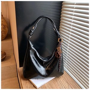 Detail of black leather hobo bag with woven strap and decorative wooden charms