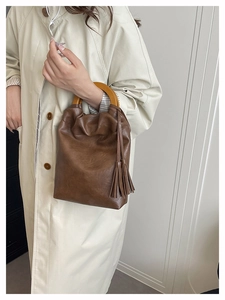Detalle del bolso saco retro marrón oscuro con asa redonda de madera y borlas de cuero