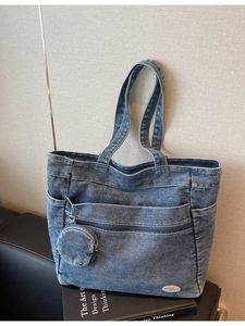 Large blue denim tote bag with multiple pockets and a round coin purse on a leather surface