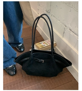 Close-up of black suede tote bag with metal buckle and long straps on wooden floor
