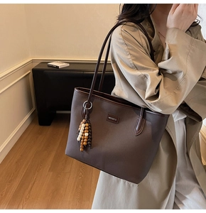 Detail of coffee brown leather tote bag with embossed logo and wooden bead charm