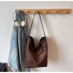 Detail of a brown suede tote bag with leather piping and a decorative bow ornament