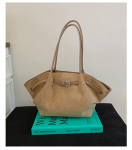 Close-up of tan suede tote bag with decorative buckle detail on green books