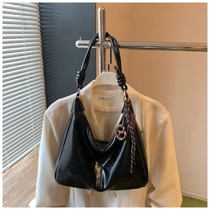Detail of glossy black shoulder bag with resin figure-eight charm and knot strap