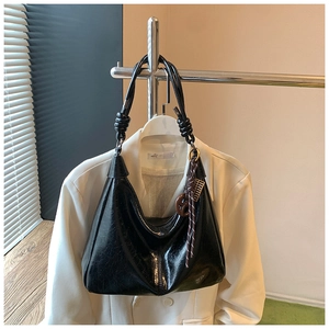 Detail of black glossy shoulder bag with unique knot strap and decorative pendant detail