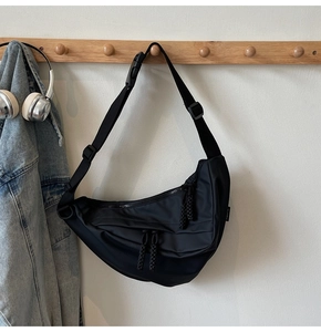 Detailansicht der schwarzen Nylon-Halbmondtasche an einem Holzhaken mit Kopfhörern daneben