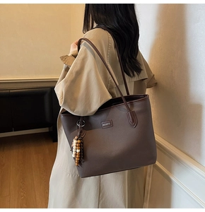 Close-up of deep brown tote bag with leather texture, brand logo, and beaded charm