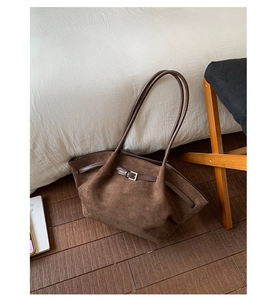 Detail of dark brown suede tote bag with slim handles and metal buckle on dark wood floor