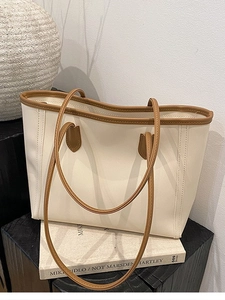 Minimalist beige tote bag with brown leather trim displayed on art books for daily commute