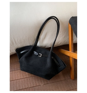 Detail of black suede tote bag showing soft texture and thin buckled strap on wood floor
