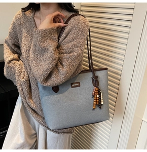 Detail einer grauen Tweed-Tasche mit Ledergriffen und bunter Perlen-Quaste am Trageriemen