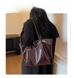 Detail of large dark brown leather tote bag with glossy finish on a shoulder