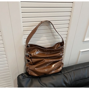 Dettaglio di borsa hobo marrone lucida con pieghe e tracolla larga su superficie
