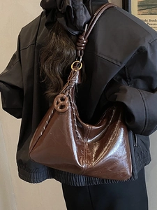 Deep brown glossy leather hobo bag with knotted strap and pretzel charm on model