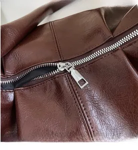 Detail of smooth metal zipper and premium leather stitching on dark brown shoulder bag