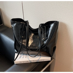 Detailed view of black patent leather tote bag showing glossy texture and strap rivets