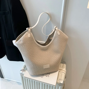 Dettaglio ravvicinato di una borsa tote intrecciata color crema con patch logo in pelle