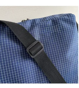 Detail of adjustable black strap and metal zipper on blue checkered canvas tote bag