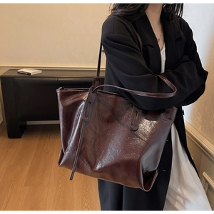 Close-up of dark brown wax leather tote bag texture with polished gloss and shoulder strap
