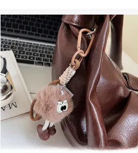 Plush brown bag charm with large eyes and cute boots hanging on a leather handbag