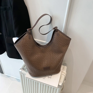Borsa tote marrone a trama intrecciata con spalline sottili su una valigia a righe