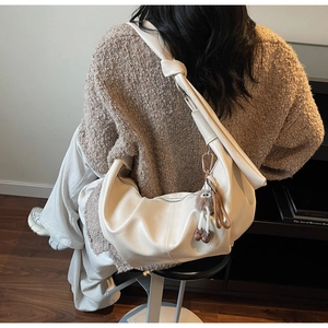 Model wearing a cream white large capacity hobo bag with knotted strap and plush charm