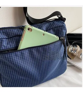 Detail of blue checkered tote bag front zipper pocket holding a green tablet device