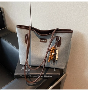 Detail der grauen Textil-Tote-Bag mit braunen Ledergriffen und Holzperlen-Quaste