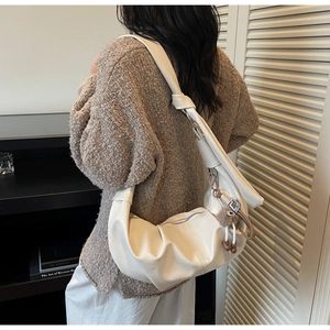 Detail of white half-moon crossbody bag with soft leather texture and pompom charm