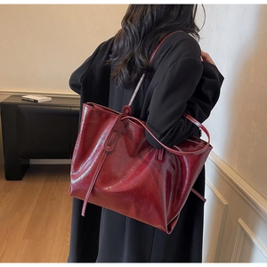 Detailed view of glossy burgundy patent leather tote bag styled on model's shoulder