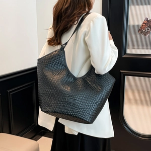 Dettaglio della borsa tote nera intrecciata con motivo a scacchi lucido su un blazer bianco