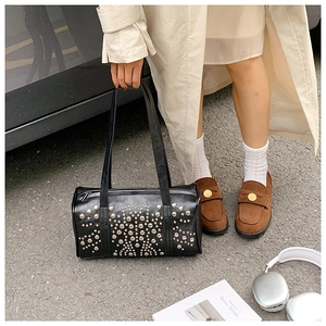 Detailed view of black cylindrical pillow bag with silver rivet patterns and chic loafers