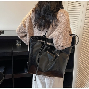 Detail of a black oversized tote bag with crinkle texture on a model shoulder