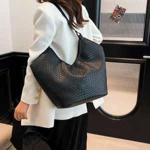 Dettaglio della trama intrecciata nera su una borsa tote grande indossata da una modella