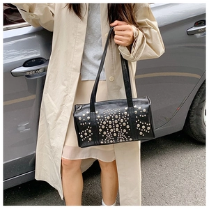 Retro studded bowling bag in shiny black leather held by a model in a beige trench coat