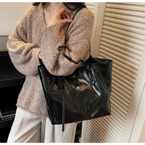Detailed close-up of glossy black leather tote bag showing fine texture and sleek strap