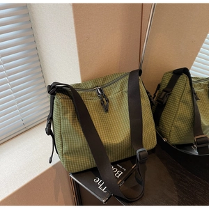 Detail view of green plaid canvas crossbody bag with adjustable wide black nylon strap