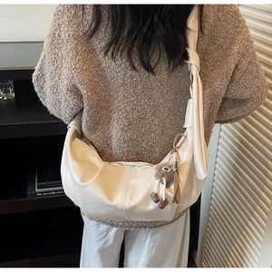 Chic beige crescent bag with knot detail and plush charm shown in a stylish outfit look