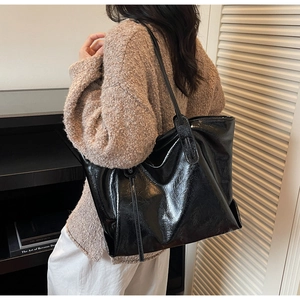 Detail of glossy black large tote bag with pleated texture worn on shoulder